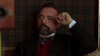 Movie still from “Topsy-Turvy” (1999), directed by Mike Leigh – A man in a suit and bow tie holding his hand up to his head; Close Up shot, Low angle