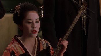 Movie still from “Topsy-Turvy” (1999), directed by Mike Leigh – A geisha is holding a guitar in her hands; Close Up shot, Over the shoulder angle
