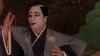 Movie still from “Topsy-Turvy” (1999), directed by Mike Leigh – A person with a face paint and a wig on; Close Up shot, Low angle