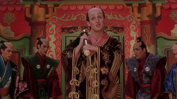 Movie still from “Topsy-Turvy” (1999), directed by Mike Leigh – A wax figure of a man in a costume holding a microphone; Medium shot, Low angle