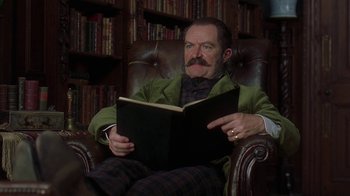 Movie still from “Topsy-Turvy” (1999), directed by Mike Leigh – A man sitting in a chair reading a book; Close Up shot, Low angle