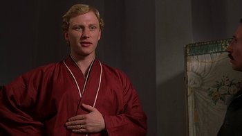 Movie still from “Topsy-Turvy” (1999), directed by Mike Leigh – A man in a red robe is holding his hands over his chest; Medium shot, Over the shoulder angle