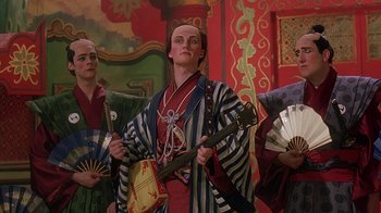 Movie still from “Topsy-Turvy” (1999), directed by Mike Leigh – A man holding a guitar in front of two other men; Medium shot, Low angle