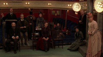 Movie still from “Topsy-Turvy” (1999), directed by Mike Leigh – A group of people sitting and standing in a room; Wide shot, High angle