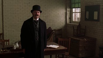 Movie still from “Topsy-Turvy” (1999), directed by Mike Leigh – A man standing in front of a table in a room; Medium shot, Low angle