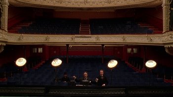 Movie still from “Topsy-Turvy” (1999), directed by Mike Leigh – Three men sitting at a table in an empty theater; Extreme Wide shot, High angle