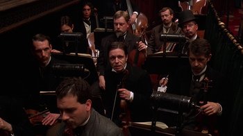 Movie still from “Topsy-Turvy” (1999), directed by Mike Leigh – A group of men in suits and hats playing musical instruments; Medium shot, High angle