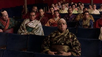 Movie still from “Topsy-Turvy” (1999), directed by Mike Leigh – A group of people sitting in a theater wearing costumes; Medium shot, High angle