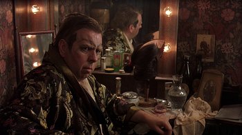 Movie still from “Topsy-Turvy” (1999), directed by Mike Leigh – A man sitting in front of a mirror in front of a bar; Close Up shot, Over the shoulder angle