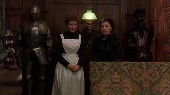 Movie still from “Topsy-Turvy” (1999), directed by Mike Leigh – Two women standing next to each other in front of a lamp; Medium shot, High angle