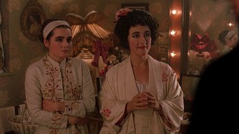 Movie still from “Topsy-Turvy” (1999), directed by Mike Leigh – Two women standing next to each other in front of a lamp; Medium shot, High angle