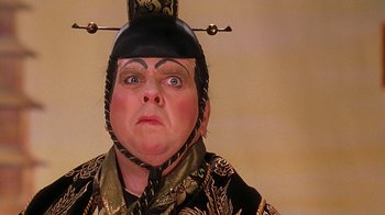 Movie still from “Topsy-Turvy” (1999), directed by Mike Leigh – A person with a hat and a black and gold outfit on; Close Up shot, Over the shoulder angle
