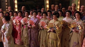 Movie still from “Topsy-Turvy” (1999), directed by Mike Leigh – A group of people standing together holding fans; Medium shot, High angle