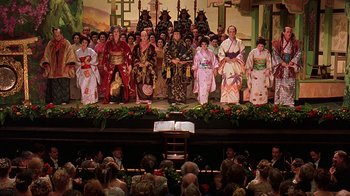 Movie still from “Topsy-Turvy” (1999), directed by Mike Leigh – A group of people in traditional japanese garb on a stage; Extreme Wide shot, High angle