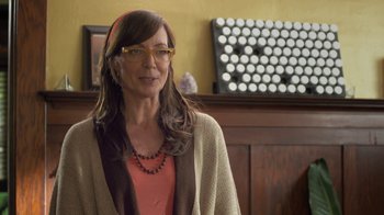 Movie still from “Touchy Feely” (2013), directed by Lynn Shelton – A woman wearing glasses standing in front of a wall; Close Up shot, Over the shoulder angle