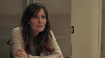 Movie still from “Touchy Feely” (2013), directed by Lynn Shelton – A woman sitting in front of a door looking at the camera; Close Up shot, Over the shoulder angle