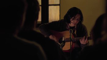 Movie still from “Touchy Feely” (2013), directed by Lynn Shelton – A person playing a guitar in front of a microphone; Medium shot, Over the shoulder angle