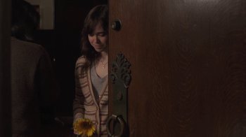 Movie still from “Touchy Feely” (2013), directed by Lynn Shelton – A woman holding a sunflower standing in front of a door; Medium shot, Over the shoulder angle
