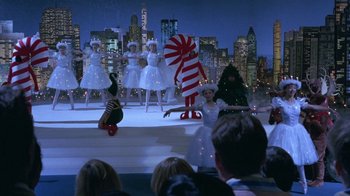 Movie still from “Toys” (1992), directed by Barry Levinson – A group of people in costumes on a stage in front of a city; Extreme Wide shot, High angle