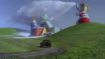 Movie still from “Toys” (1992), directed by Barry Levinson – A car driving down a road in a grassy area; Extreme Wide shot, Low angle