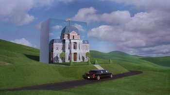 Movie still from “Toys” (1992), directed by Barry Levinson – A car driving down a road next to a painting of a house; Extreme Wide shot, High angle