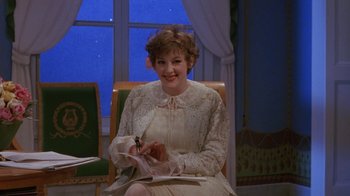 Movie still from “Toys” (1992), directed by Barry Levinson – A woman in a white dress is writing on a piece of paper in front of a window; Medium shot, High angle