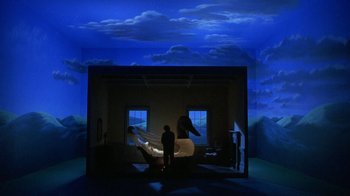 Movie still from “Toys” (1992), directed by Barry Levinson – A man standing in front of a painting of a swan; Extreme Wide shot, High angle