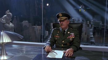 Movie still from “Toys” (1992), directed by Barry Levinson – A man in a military uniform sitting at a desk; Wide shot, Low angle