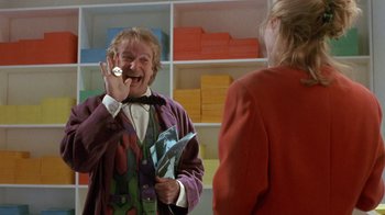 Movie still from “Toys” (1992), directed by Barry Levinson – A man in a suit and tie and a woman in a red jacket; Medium shot, Over the shoulder angle