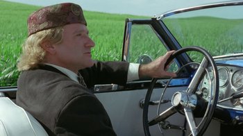Movie still from “Toys” (1992), directed by Barry Levinson – A man driving a truck in a field; Medium shot, Low angle