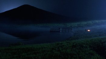 Movie still from “Toys” (1992), directed by Barry Levinson – A person standing on a dock in a body of water at night; Extreme Wide shot, High angle