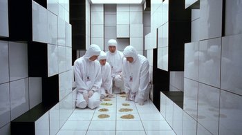 Movie still from “Toys” (1992), directed by Barry Levinson – A group of people in white suits sitting in a room; Wide shot, Overhead angle