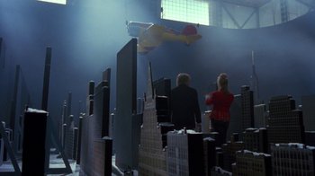 Movie still from “Toys” (1992), directed by Barry Levinson – Two people are standing in front of a model of a skyscraper; Extreme Wide shot, Low angle