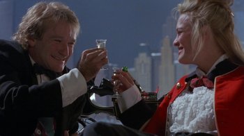 Movie still from “Toys” (1992), directed by Barry Levinson – A man and a woman sitting next to each other holding wine glasses; Close Up shot, Low angle