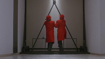 Movie still from “Toys” (1992), directed by Barry Levinson – Two men in red coats standing in front of a wall; Wide shot, Low angle