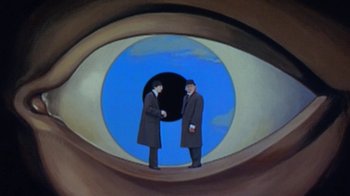 Movie still from “Toys” (1992), directed by Barry Levinson – Two men shaking hands in front of an image of an eye; Wide shot, Overhead angle