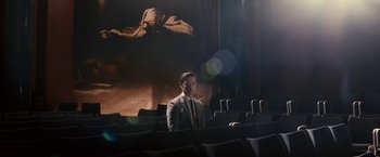Movie still from “Trance” (2013), directed by Danny Boyle – A man in a suit sitting in front of a painting; Extreme Wide shot, Low angle