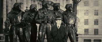 Movie still from “Trance” (2013), directed by Danny Boyle – A man in a suit standing in front of a group of statues; Medium shot, Low angle