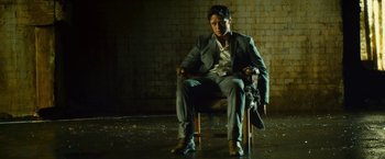 Movie still from “Trance” (2013), directed by Danny Boyle – A man in a suit sitting in a chair; Medium shot, Low angle