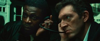 Movie still from “Trance” (2013), directed by Danny Boyle – Two men looking at each other with one holding a microphone; Close Up shot, Low angle