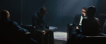 Movie still from “Trance” (2013), directed by Danny Boyle – A man sitting on a chair in a dark room; Medium shot, Over the shoulder angle