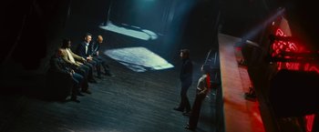 Movie still from “Trance” (2013), directed by Danny Boyle – A group of people standing on a stage in front of a projector; Wide shot, High angle