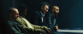 Movie still from “Trance” (2013), directed by Danny Boyle – A group of men sitting next to each other in a room; Medium shot, Low angle