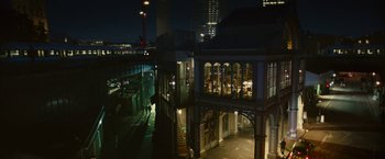 Movie still from “Trance” (2013), directed by Danny Boyle – A night view of a building with a person walking on the sidewalk; Extreme Wide shot, High angle
