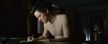 Movie still from “Trance” (2013), directed by Danny Boyle – A shirtless man writing on top of a table; Medium shot, High angle