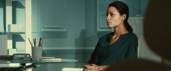 Movie still from “Trance” (2013), directed by Danny Boyle – A woman sitting at a table in front of a book; Medium shot, Over the shoulder angle