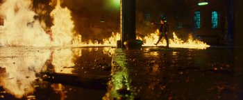 Movie still from “Trance” (2013), directed by Danny Boyle – A man walking on a sidewalk near a fire; Extreme Wide shot, Low angle