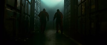 Movie still from “Transporter 3” (2008), directed by Olivier Megaton – Two men in orange suits are walking through a dark hallway; Medium shot, Low angle