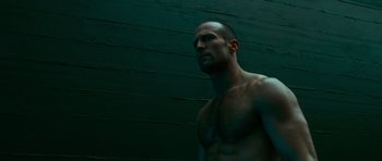 Movie still from “Transporter 3” (2008), directed by Olivier Megaton – A man with no shirt standing in front of a green wall; Close Up shot, Low angle