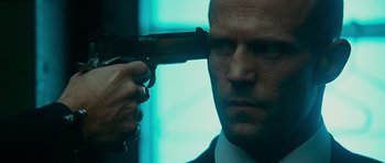 Movie still from “Transporter 3” (2008), directed by Olivier Megaton – A man holding a gun up to his face; Close Up shot, Over the shoulder angle